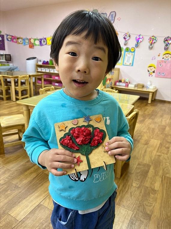 A little boy proudly holding up a construction-paper flower craft he made