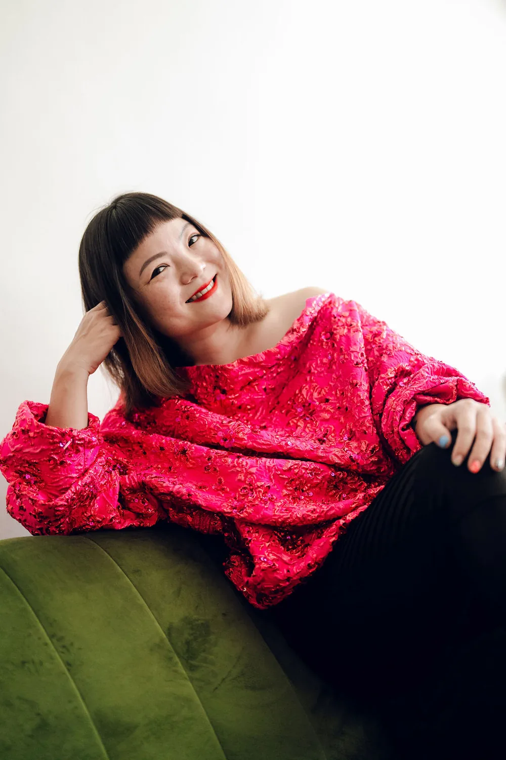 Simone Grace Seol, leaning back and smiling on a green velvet couch